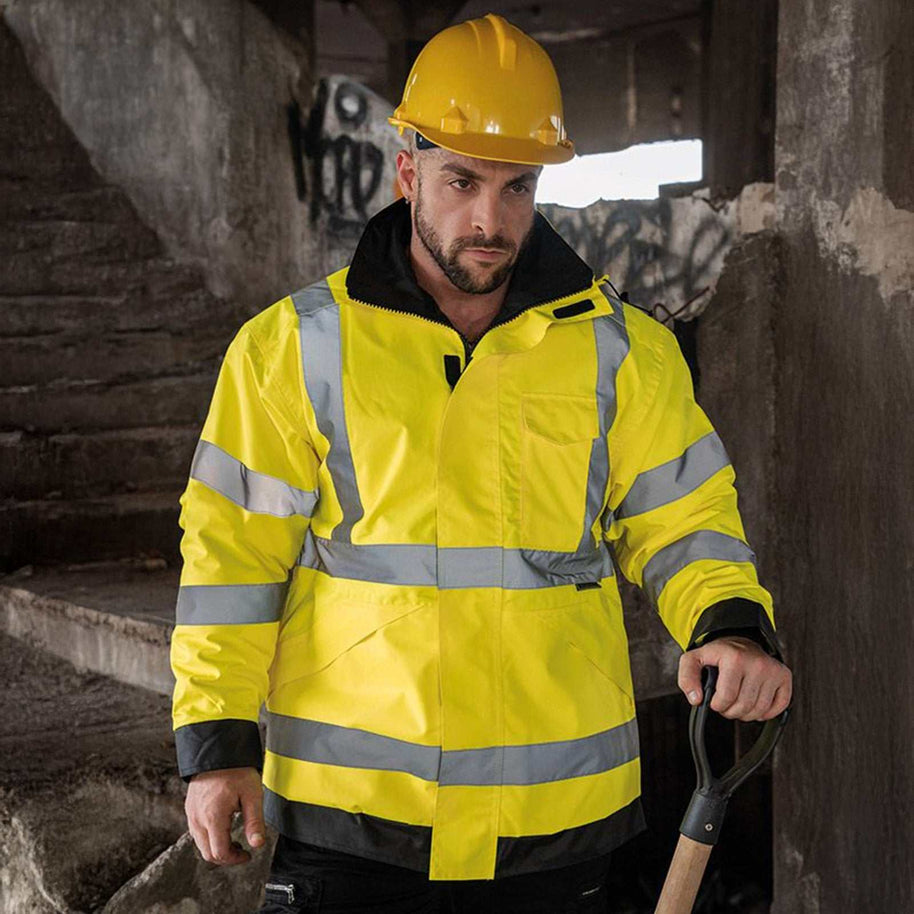 Mann trägt gelbe Regenjacke Lite Kaunas mit vier reflektierenden Leuchtstreifen und Schutzhelm auf Baustelle